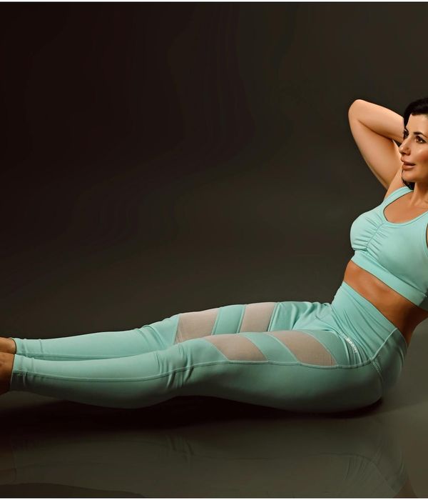 Woman in a calm yoga pose in a dark studio with cyan light.